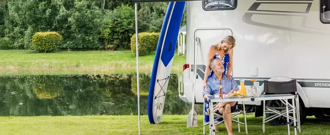 Sfeerbeeld van een stel dat buiten zit met de camper erachter en met veel groen op de achtegrond