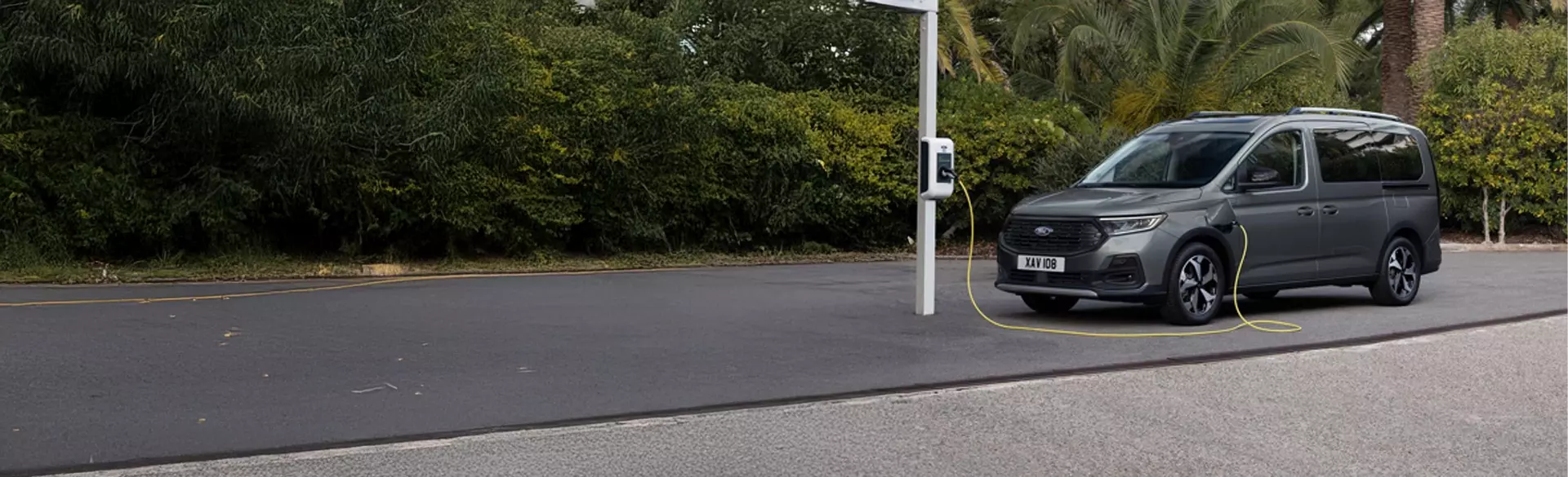 Ford Tourneo Connect Plug-in Hybrid opgeladen bij een openbare laadpaal in een groene, rustige omgeving.